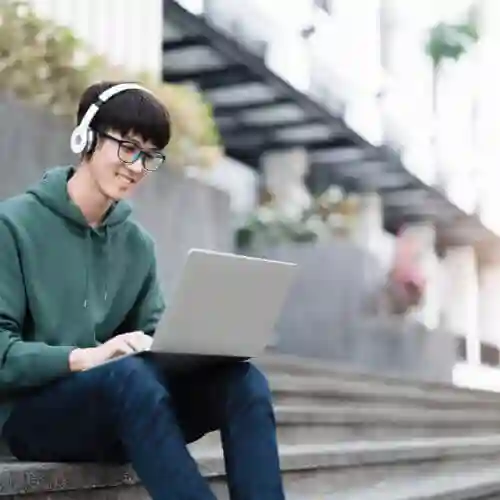 A STUDENT USES LAPTO ON STAIR WITH HEAD PHONE